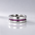 A polished silver-tone ring featuring a channel-set row of small pink gemstones, displayed on a reflective light gray surface.