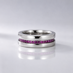 A polished silver-tone ring featuring a channel-set row of small pink gemstones, displayed on a reflective light gray surface.