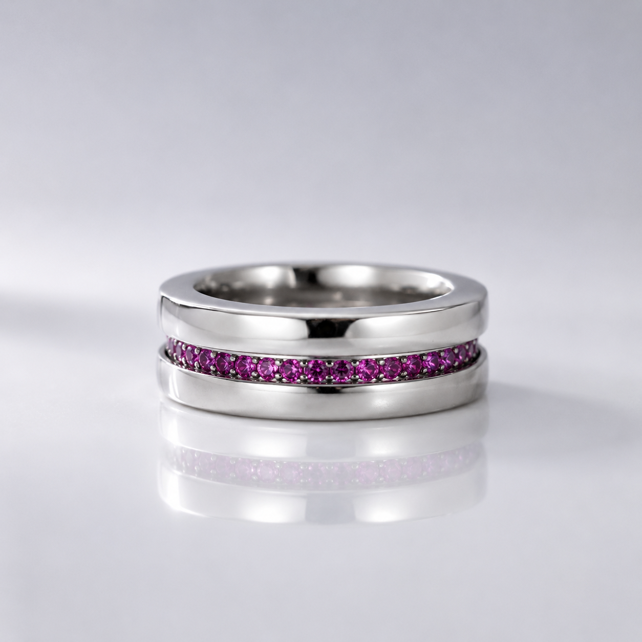 A polished silver-tone ring featuring a channel-set row of small pink gemstones, displayed on a reflective light gray surface.