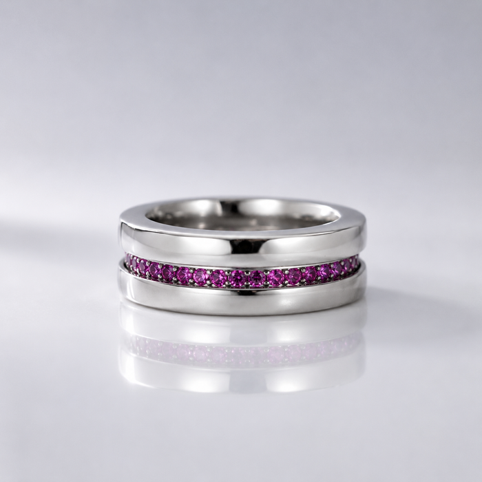 A polished silver-tone ring featuring a channel-set row of small pink gemstones, displayed on a reflective light gray surface.