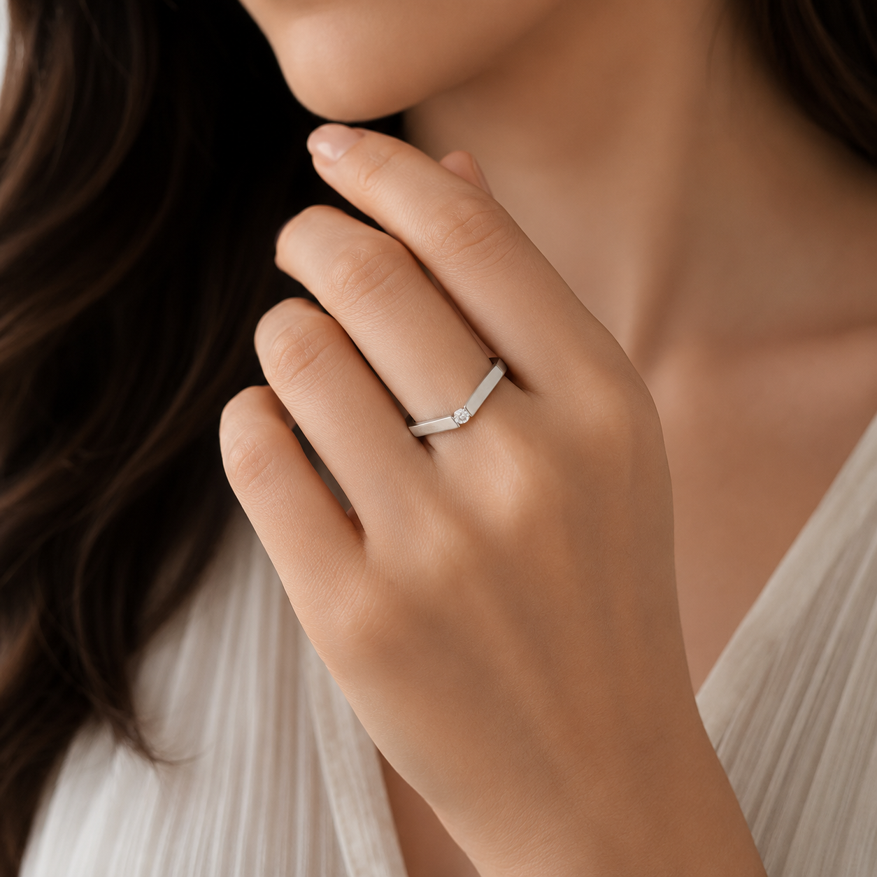 A close-up lifestyle shot of a woman wearing a slim silver band ring with a small round clear gemstone on her finger.