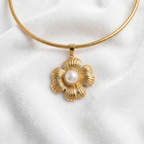 A gold snake-chain necklace with a textured gold flower pendant featuring a white faux-pearl center, displayed on a soft white fabric background.