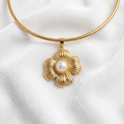 A gold snake-chain necklace with a textured gold flower pendant featuring a white faux-pearl center, displayed on a soft white fabric background.