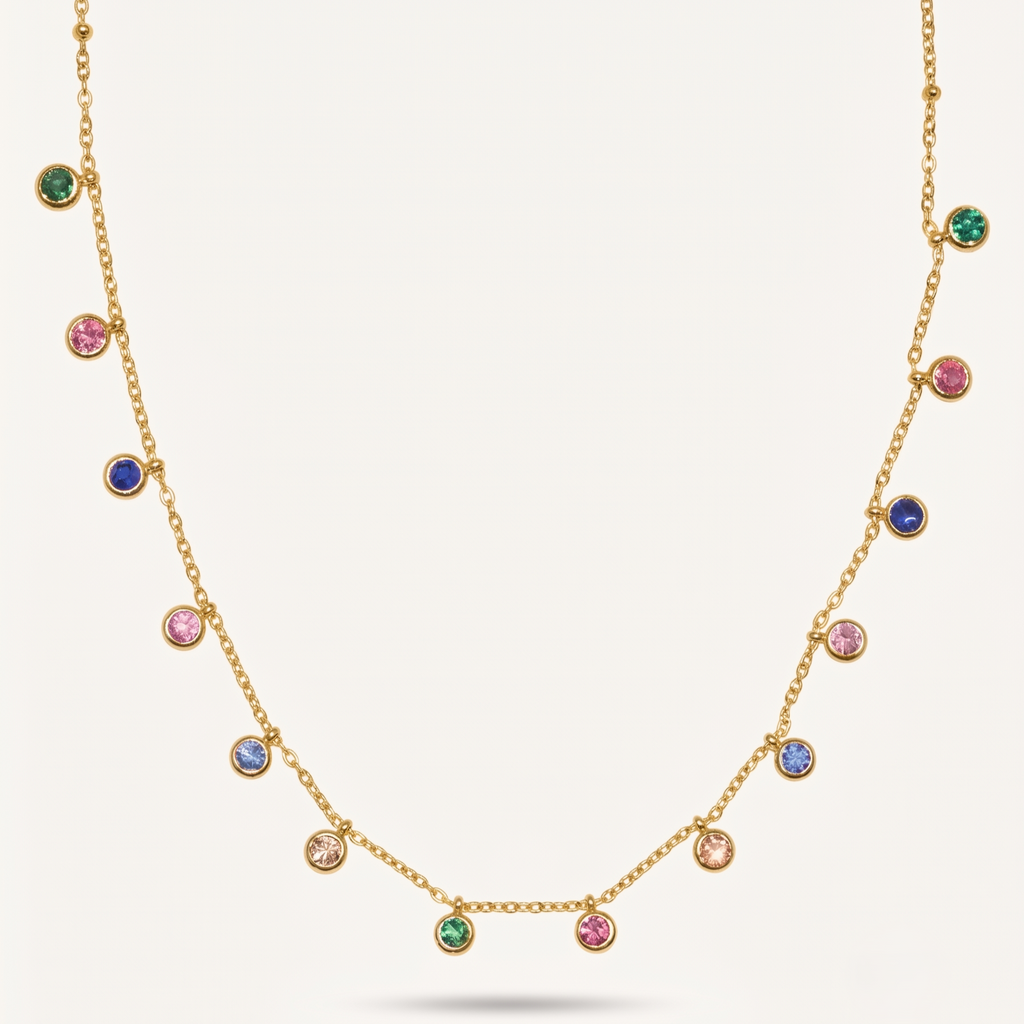 A gold chain necklace featuring multiple small round bezel-set gemstones in green, pink, blue, and clear, displayed against a light cream background.